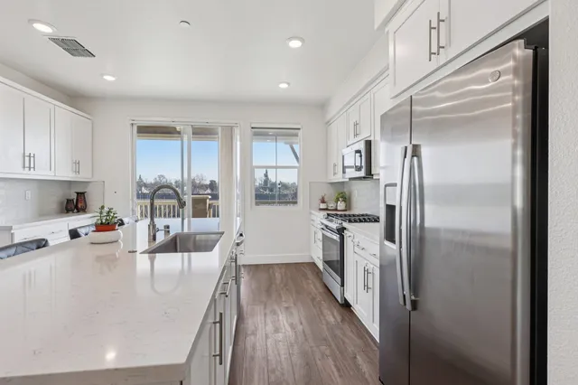 a large kitchen with stainless steel appliances a refrigerator a sink dishwasher a stove and white cabinets with wooden floor