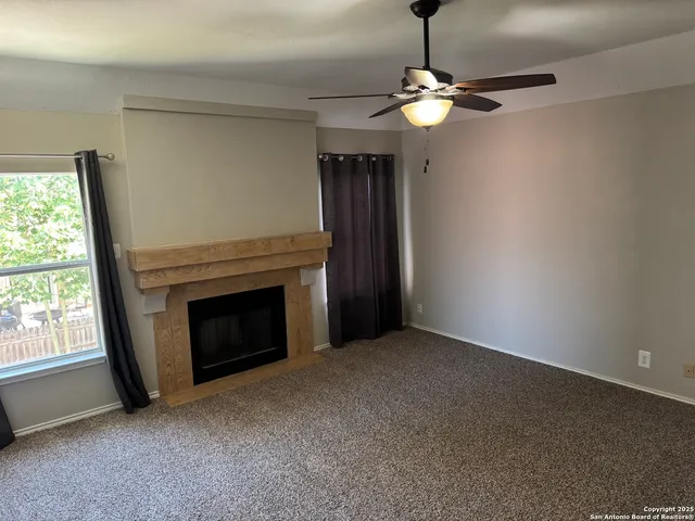 a view of an empty room with chandelier fan and fire place