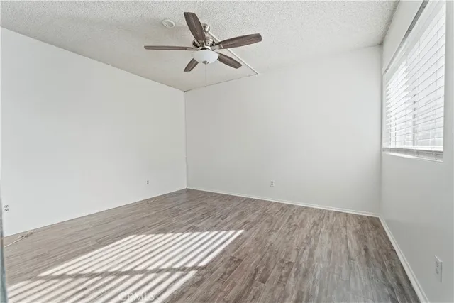 an empty room with wooden floor a ceiling fan and windows