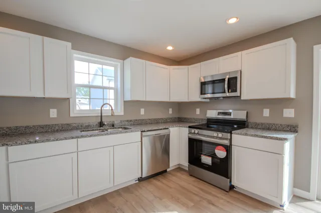 a kitchen with stainless steel appliances granite countertop white cabinets a sink a stove a microwave and wooden floors