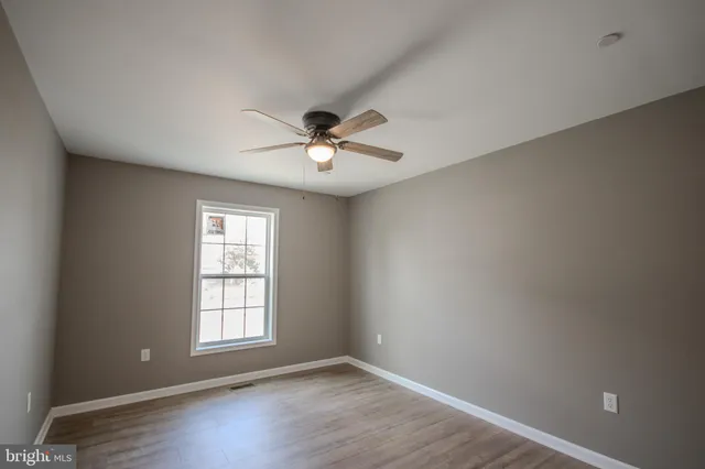 an empty room with wooden floor chandelier fan and windows