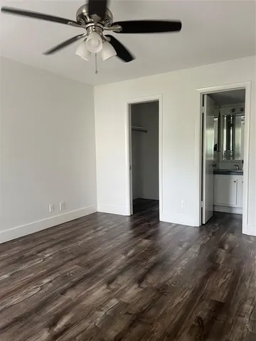 a view of an empty room with wooden floor and a ceiling fan