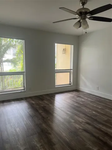 an empty room with wooden floor fan and windows