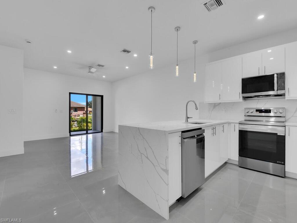 4450-4452 24th Street Southwest Lehigh Acres, FL 33973 - Photo 32 of 49 a kitchen with stainless steel appliances kitchen island granite countertop a stove a sink and a microwave