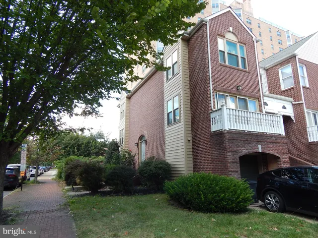 a view of a brick house with a yard plants and a large tree