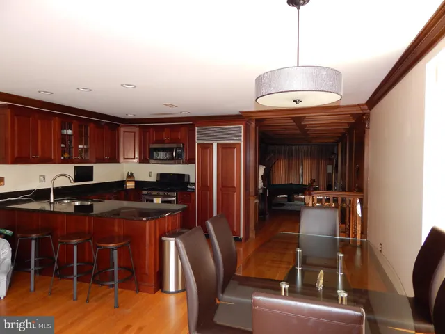 a kitchen with stainless steel appliances granite countertop a stove top oven a sink a dining table and chairs with wooden floor