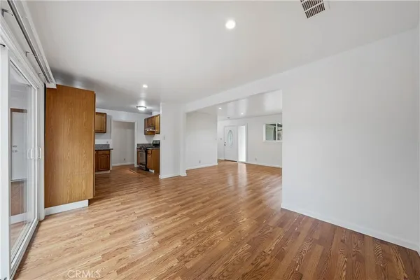 a view of empty room with wooden floor and kitchen