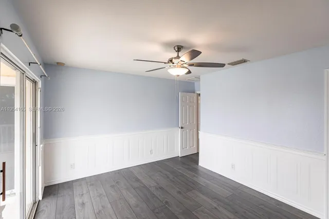 an empty room with wooden floor chandelier fan and windows