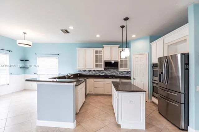 a kitchen with stainless steel appliances granite countertop a refrigerator a sink dishwasher a stove and white cabinets with wooden floor