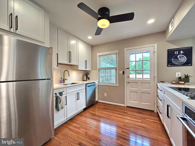 a kitchen with stainless steel appliances granite countertop a refrigerator a stove a sink and white cabinets with wooden floor