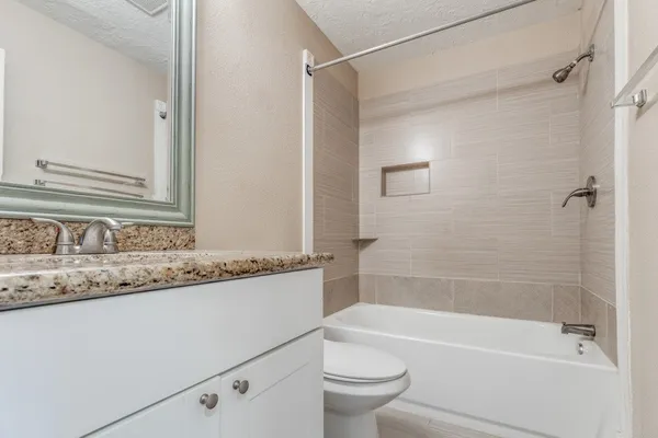 a bathroom with a granite countertop bathtub shower sink vanity and toilet