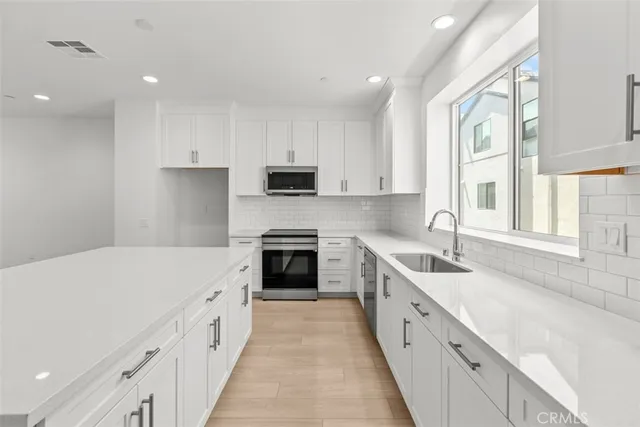 a large white kitchen with granite countertop a sink and dishwasher a stove top oven with wooden floor