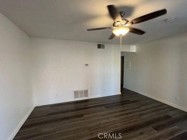 a view of an empty room with wooden floor and a ceiling fan