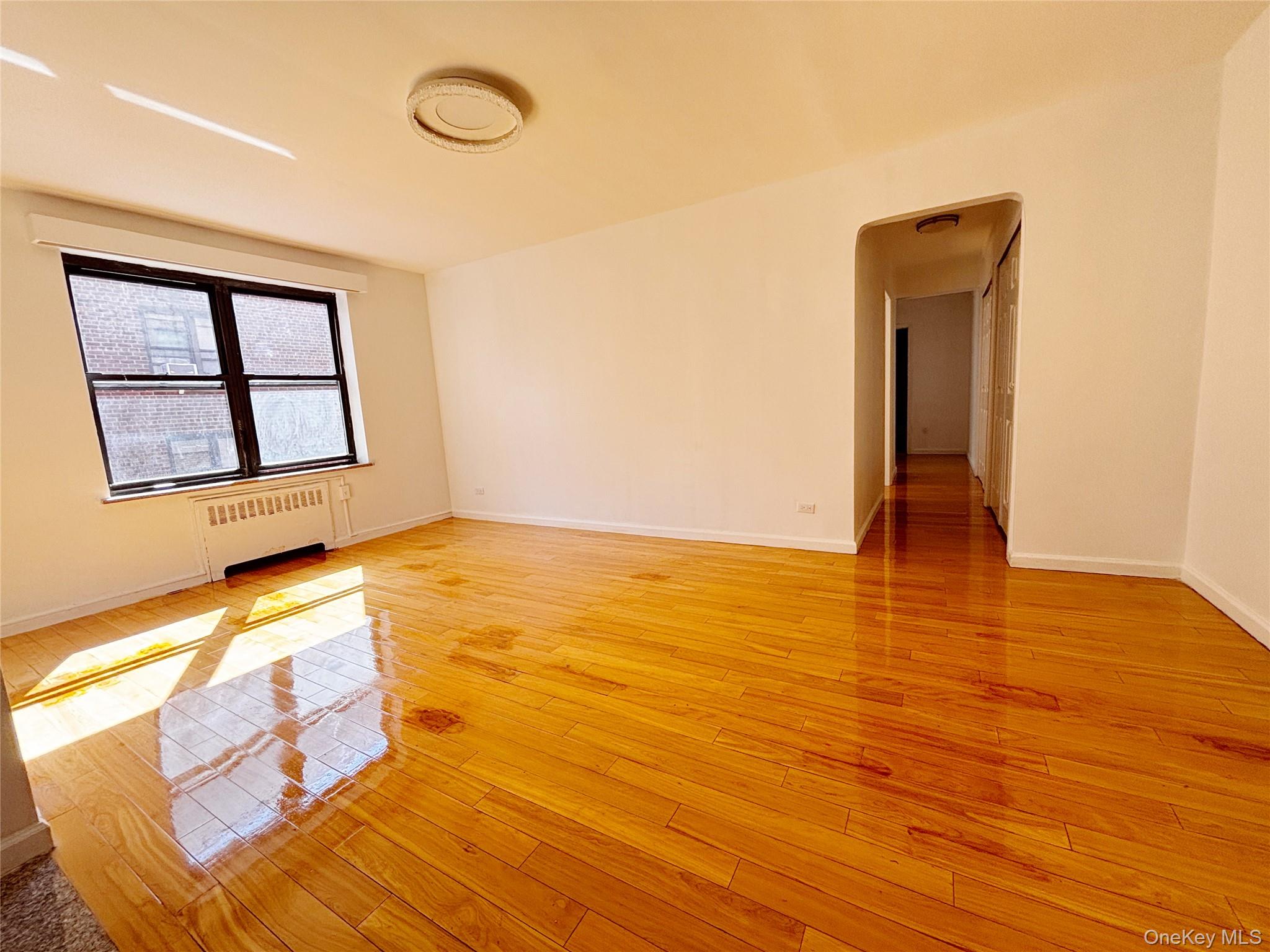 44-25 Macnish Street, Unit 4A Queens, NY 11373 - Photo 4 of 12 Empty room featuring radiator, light wood finished floors, and arched walkways