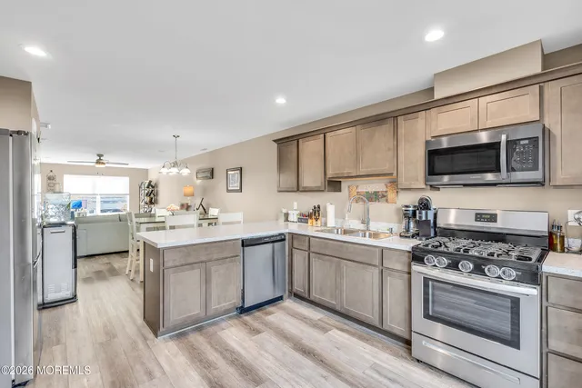 a kitchen with stainless steel appliances granite countertop a stove top oven a sink dishwasher and a refrigerator with wooden floor