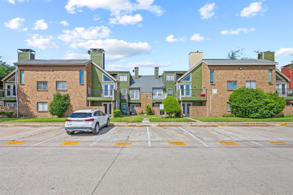 9837 Walnut Street, Unit S203 Dallas, TX 75243 - Photo 26 of 26 The property features a brick exterior with green siding and balconies, alongside a dedicated parking lot