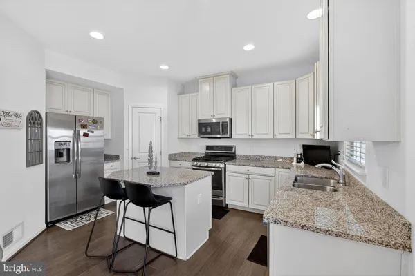 a kitchen with stainless steel appliances granite countertop a sink a stove a refrigerator cabinets and a dining table with wooden floor
