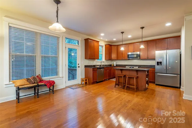 a kitchen with stainless steel appliances kitchen island granite countertop a refrigerator a stove a sink dishwasher with a dining table and chairs with wooden floor