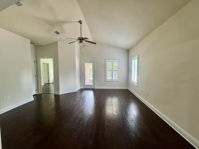 an empty room with wooden floor chandelier fan and windows