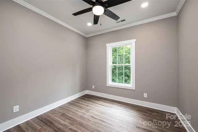 an empty room with wooden floor chandelier fan and windows