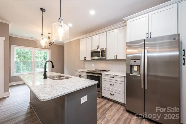 a kitchen with stainless steel appliances granite countertop a refrigerator a sink dishwasher a stove and a dining table with wooden floor