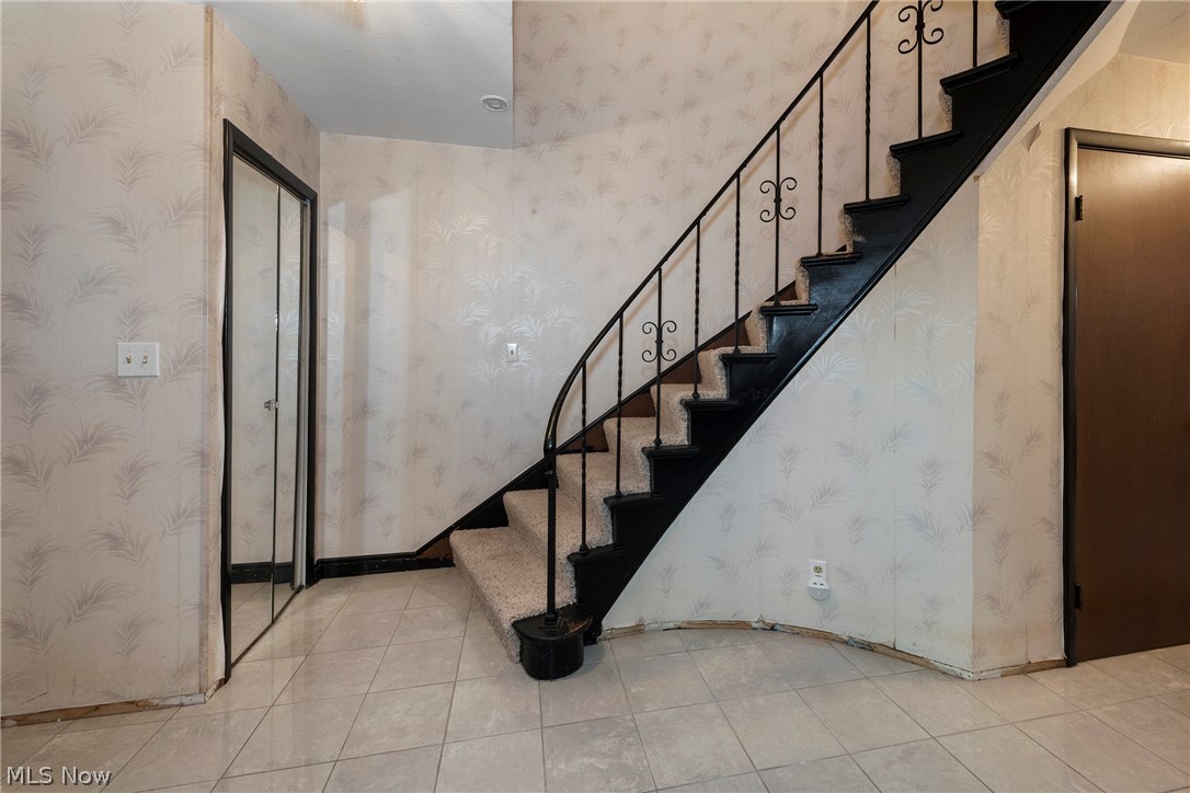 6484 State Road Parma, OH 44134 - Photo 8 of 36 Welcoming foyer featuring tile flooring, mirrored closet doors, and a decorative staircase railing.