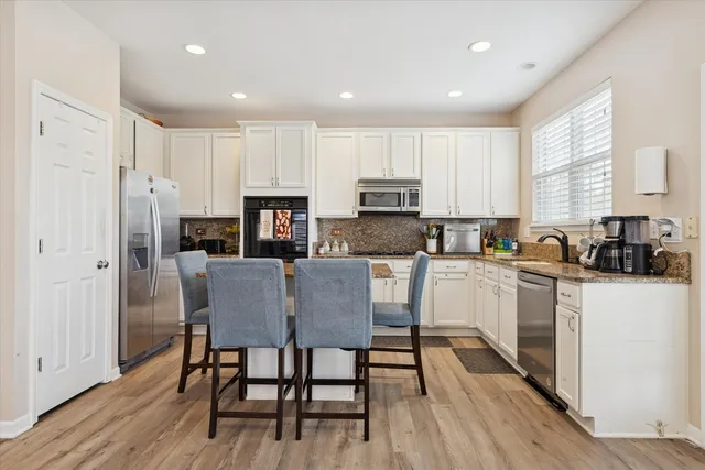 a kitchen with stainless steel appliances granite countertop a refrigerator a stove top oven a sink dishwasher a dining table and chairs with wooden floor