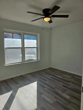 an empty room with wooden floor fan and windows
