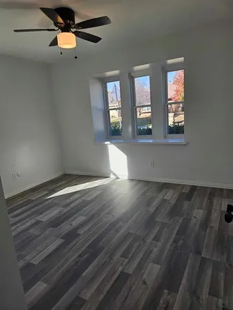 an empty room with wooden floor chandelier fan and windows