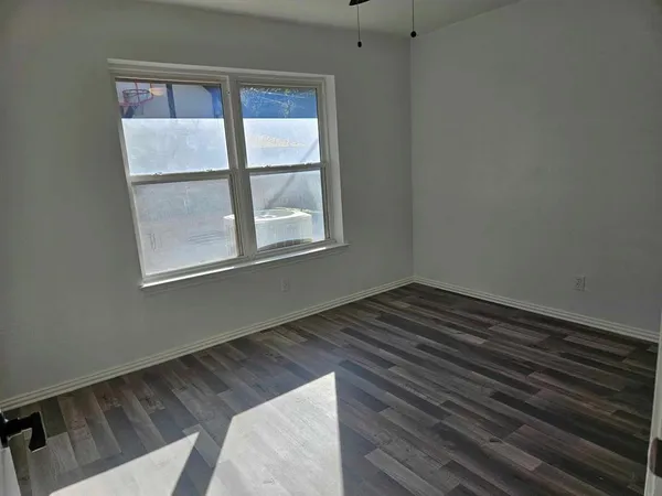 a view of an empty room with wooden floor and a window