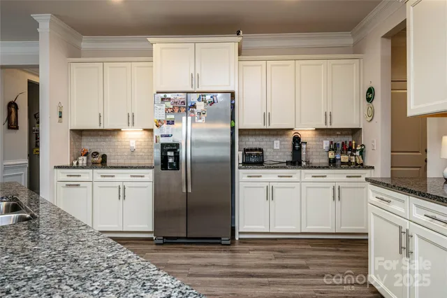 a kitchen with granite countertop a refrigerator sink and white cabinets