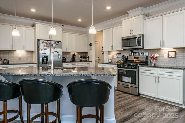 a kitchen with stainless steel appliances granite countertop a stove top oven a sink a dining table and chairs with wooden floor