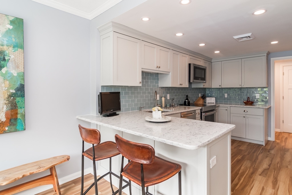 75 Grove Street, Unit 124 Wellesley, MA 02482 - Photo 5 of 22 a kitchen with stainless steel appliances granite countertop a sink a stove a microwave a island with a dining table and chairs