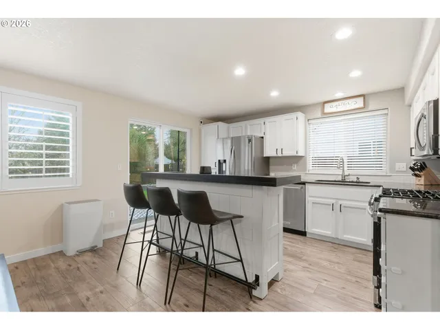 a kitchen with stainless steel appliances granite countertop a stove a sink a refrigerator white cabinets and a dining table with wooden floor