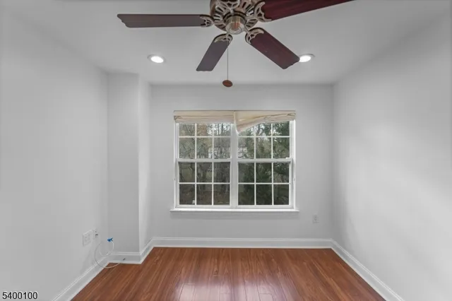 an empty room with wooden floor chandelier fan and windows