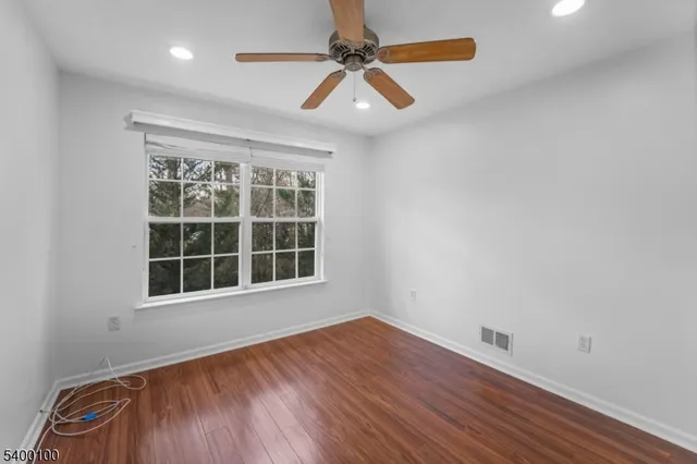 an empty room with wooden floor ceiling fan and windows