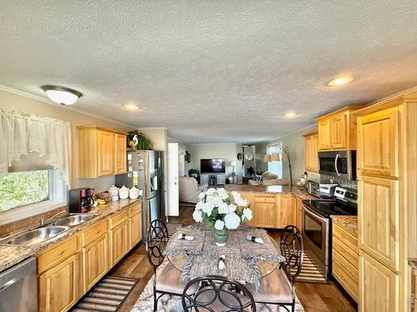 a kitchen with stainless steel appliances kitchen island granite countertop a refrigerator oven a stove top oven a sink dishwasher and dining table with wooden floor
