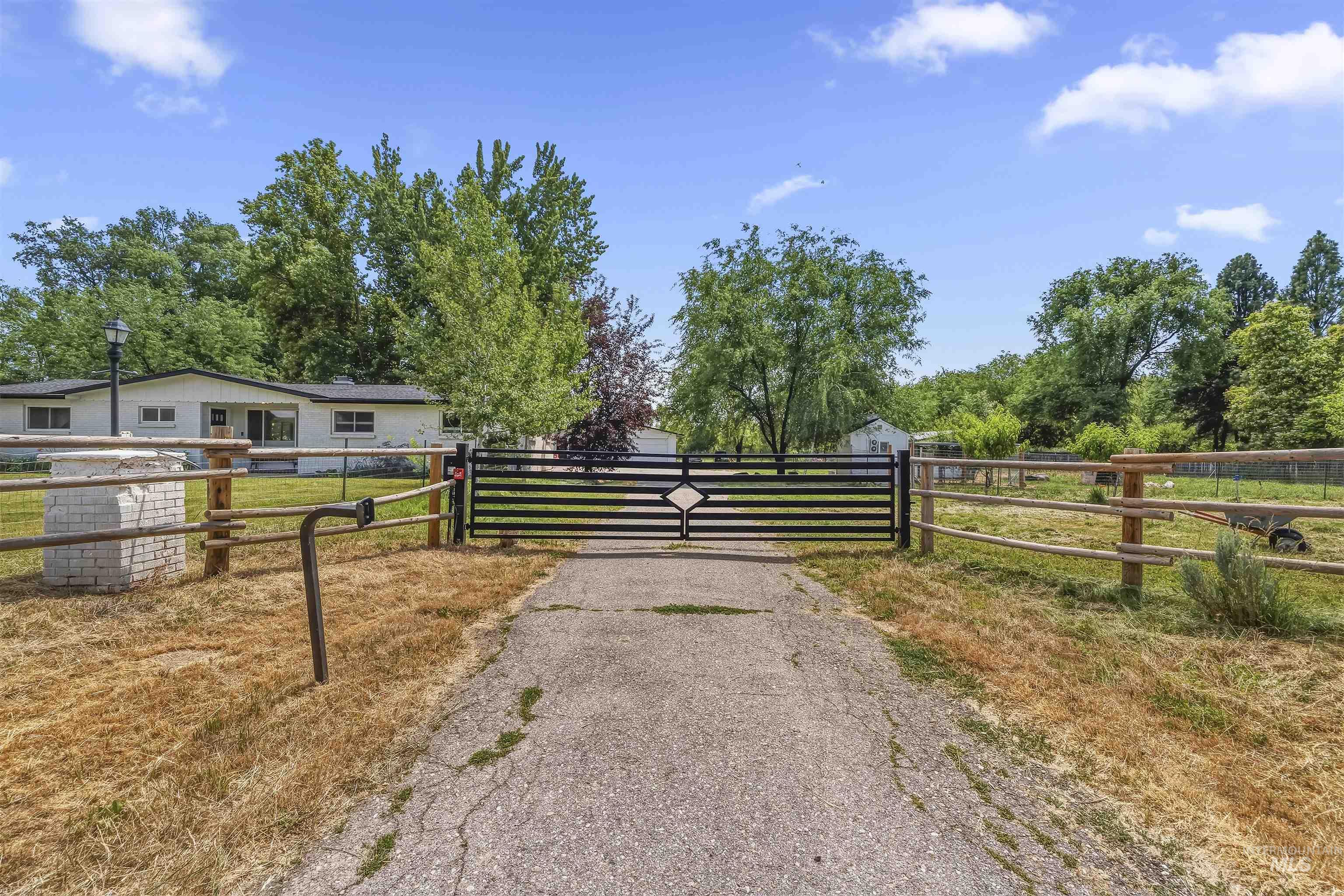 355 East Beacon Light Road Eagle, ID 83616 - Photo 42 of 47 Paved driveway entry with a decorative metal gate, flanked by a white brick column and split-rail fencing