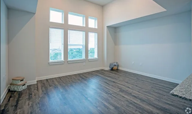 an empty room with wooden floor fan and windows