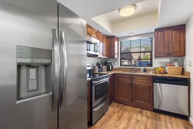 a kitchen with stainless steel appliances granite countertop a refrigerator a sink dishwasher a stove and white countertops with wooden floor