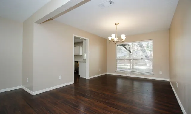 an empty room with wooden floor chandelier and windows