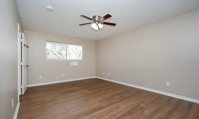 an empty room with wooden floor fan and windows