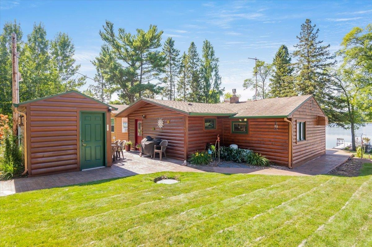 Back of property featuring faux log siding, a shed, a chimney, and a yard
