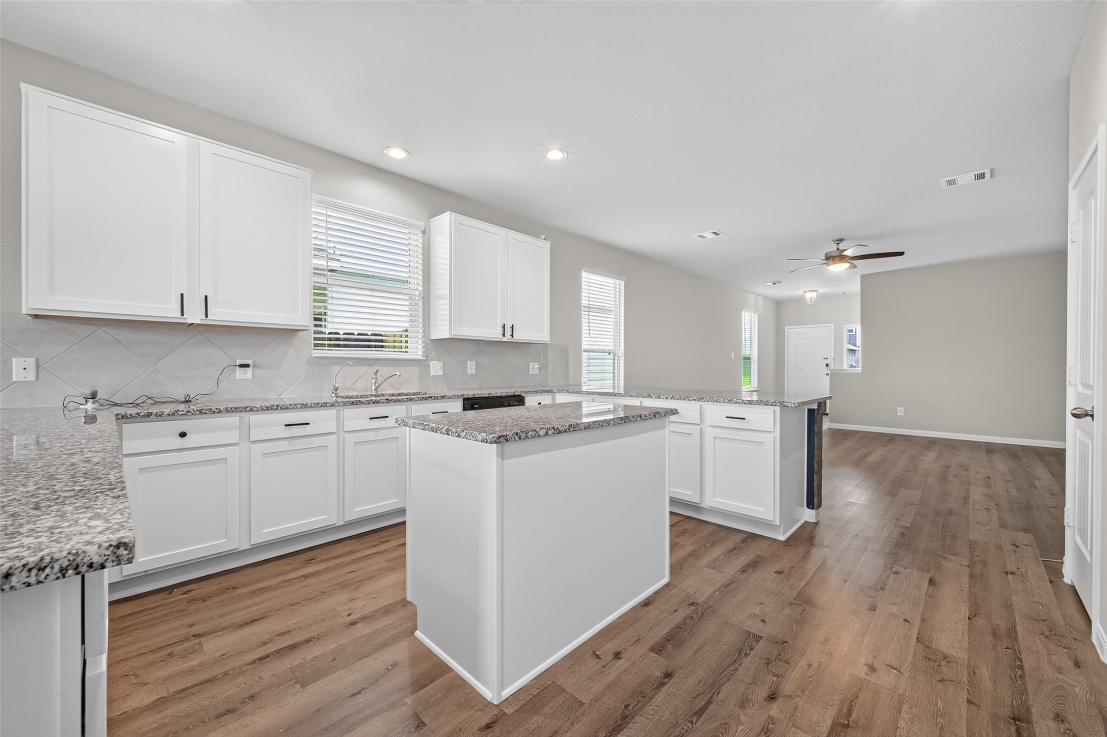2526 Sturgeon Way Conroe, TX 77384 - Photo 6 of 49 This photo showcases a spacious open-concept kitchen and living area with wood flooring. The kitchen features white cabinets, granite countertops, and an island, while the living area includes ceiling fans and ample natural light from multiple windows.