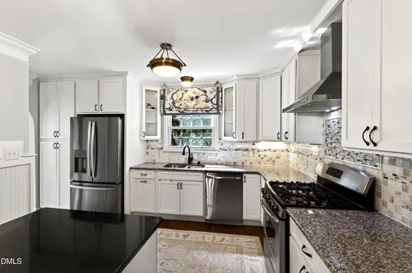 a kitchen with stainless steel appliances granite countertop a stove a sink dishwasher and a dining table with wooden floor