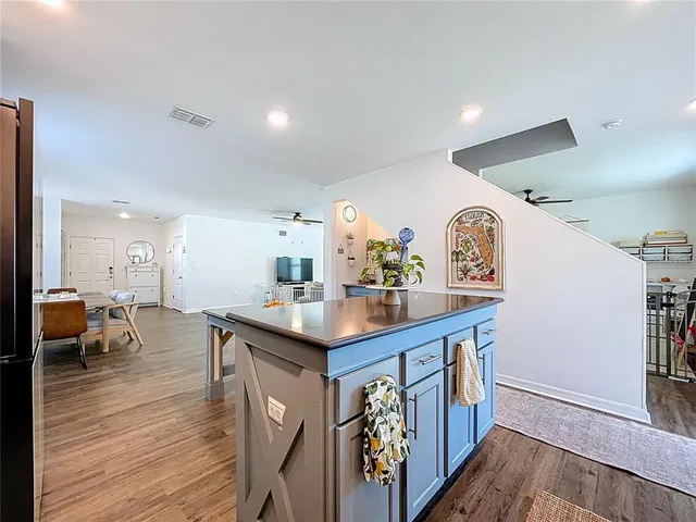 a kitchen with stainless steel appliances kitchen island granite countertop a refrigerator a stove a sink a dining table and chairs with wooden floor
