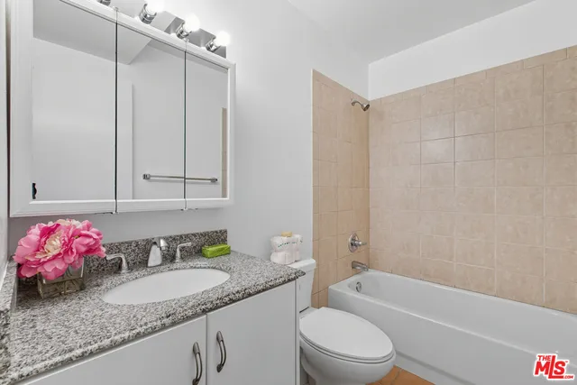 a bathroom with a granite countertop bathtub sink vanity mirror and toilet