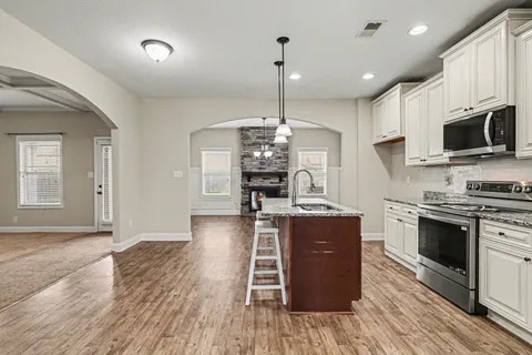 a kitchen with kitchen island granite countertop a stove top oven a sink dishwasher a dining table and chairs with wooden floor