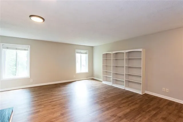 an empty room with wooden floor fireplace and windows