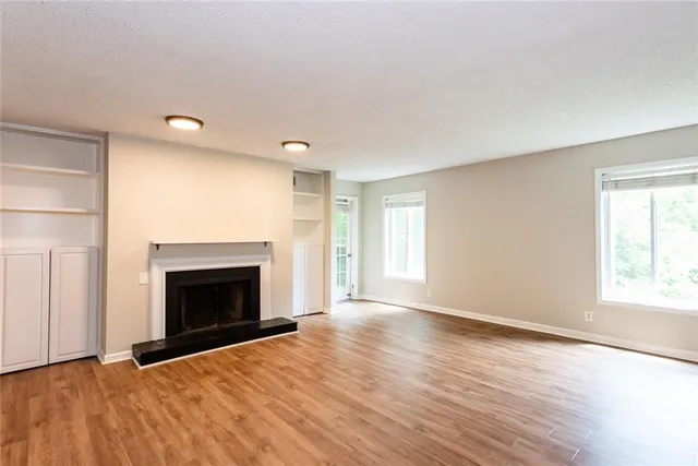 an empty room with wooden floor fireplace and windows